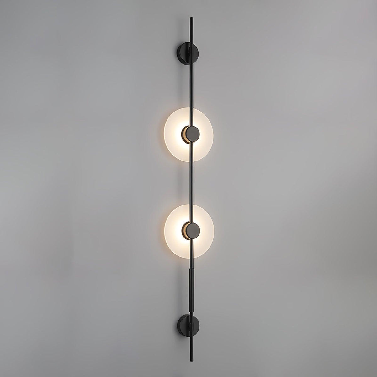 Close front view of this Clérachic sconce in black, two lit alabaster discs on a rod against a plain grey wall.