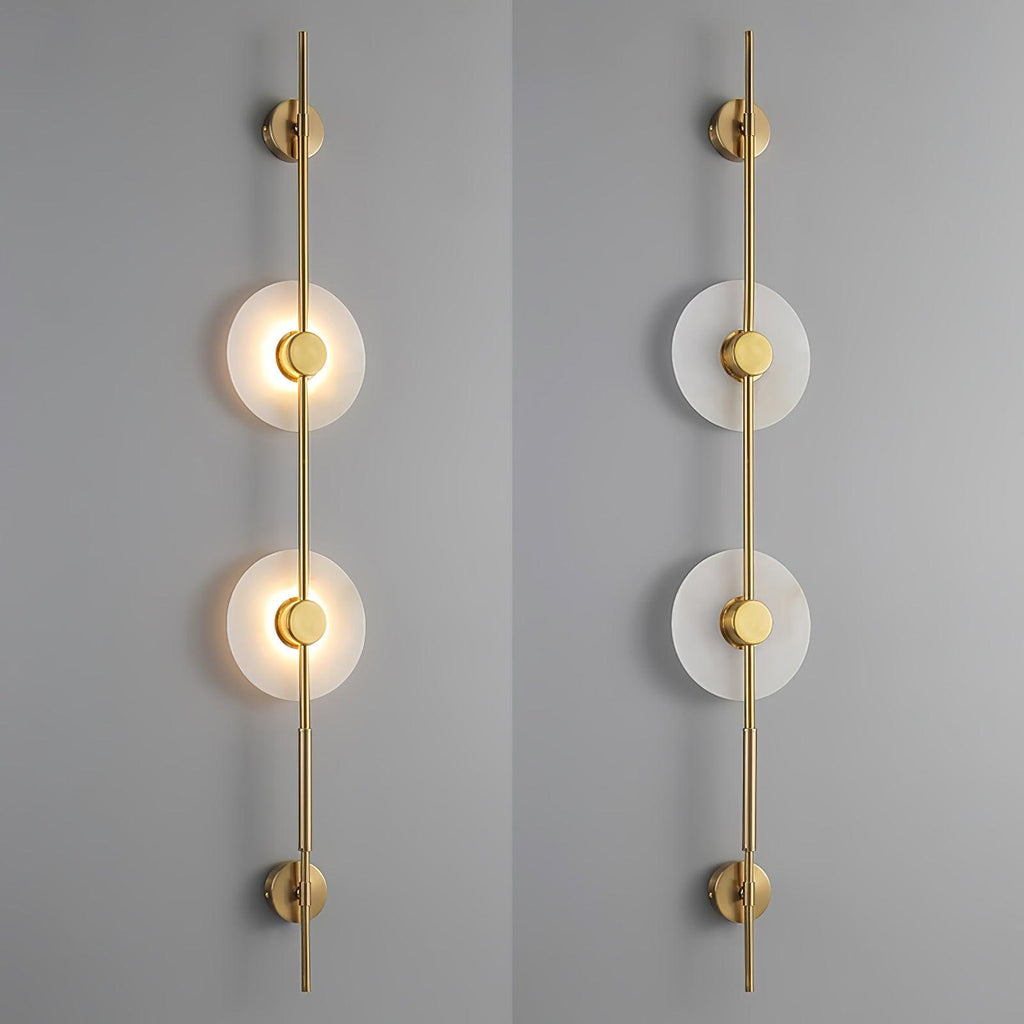 Two gold Clérachic sconces side by side, one with its discs lit and one unlit, against a grey wall.