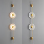 Two gold Clérachic sconces side by side, one with its discs lit and one unlit, against a grey wall.