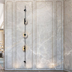 Tall black three-disc Clérachic sconce on a grey marble-look panel with fine gold veining, its discs glowing.