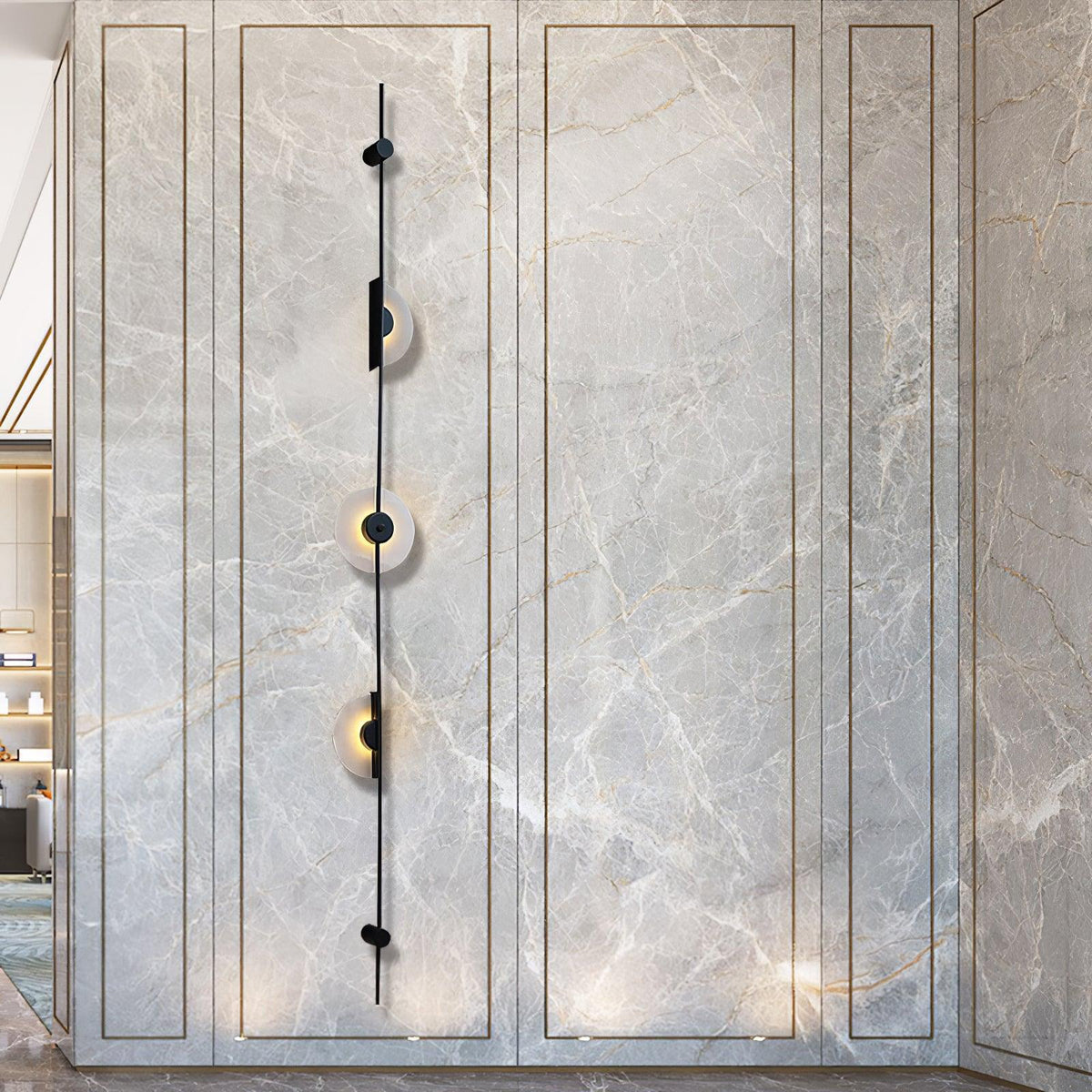 Tall black three-disc Clérachic sconce on a grey marble-look panel with fine gold veining, its discs glowing.