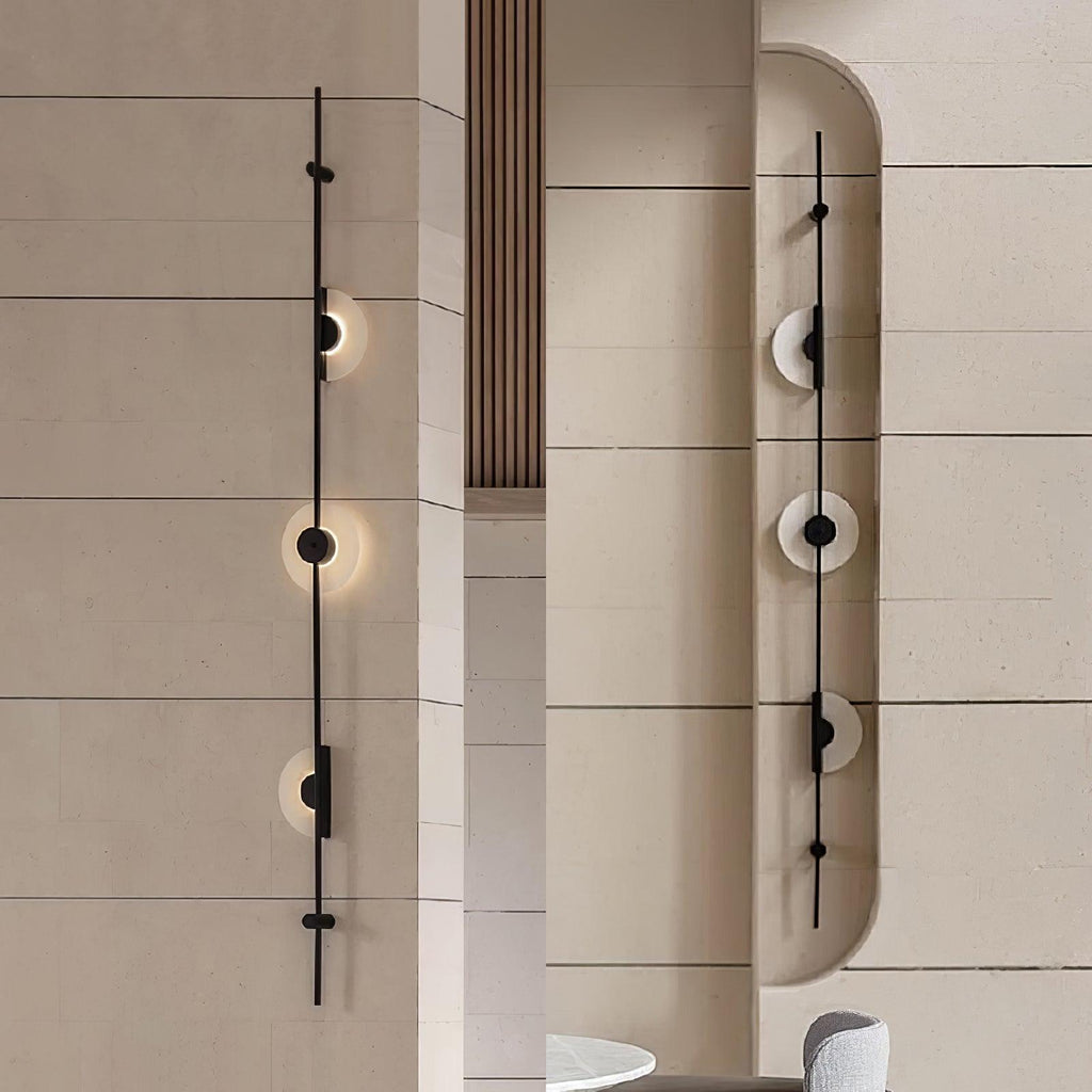 Two black three-disc Clérachic sconces on stone-clad walls, one on a flat wall and one in a curved niche, both lit.
