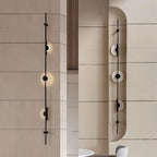 Two black three-disc Clérachic sconces on stone-clad walls, one on a flat wall and one in a curved niche, both lit.