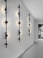 Three black Clérachic sconces on a long white corridor wall, their alabaster discs glowing, with a framed portrait at the right.