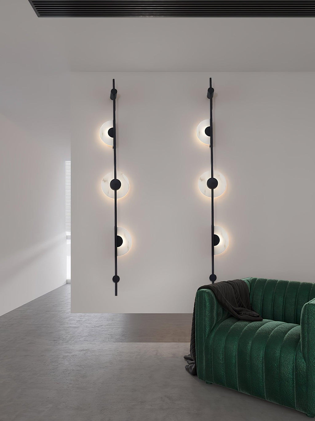Two black three-disc Clérachic sconces on a white wall by a green velvet sofa, with all the discs lit.