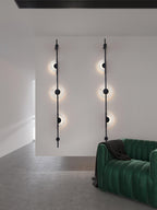 Two black three-disc Clérachic sconces on a white wall by a green velvet sofa, with all the discs lit.