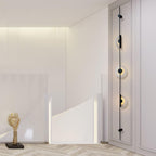Black three-disc Clérachic sconce on a white panelled wall beside a staircase balustrade and a small gold sculpture.