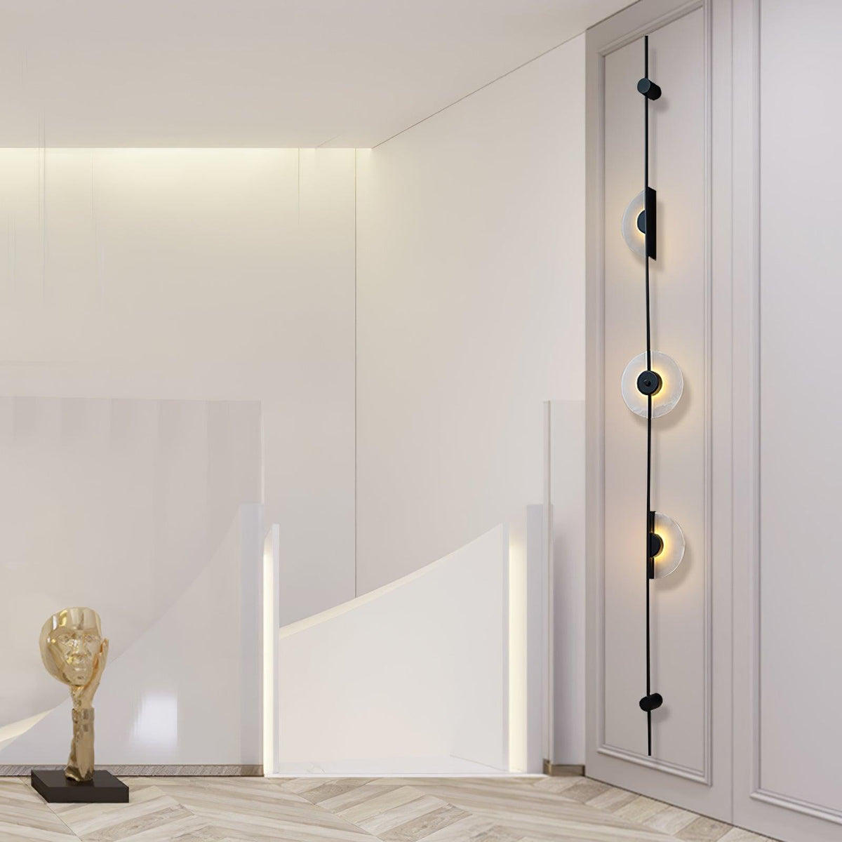 Black three-disc Clérachic sconce on a white panelled wall beside a staircase balustrade and a small gold sculpture.