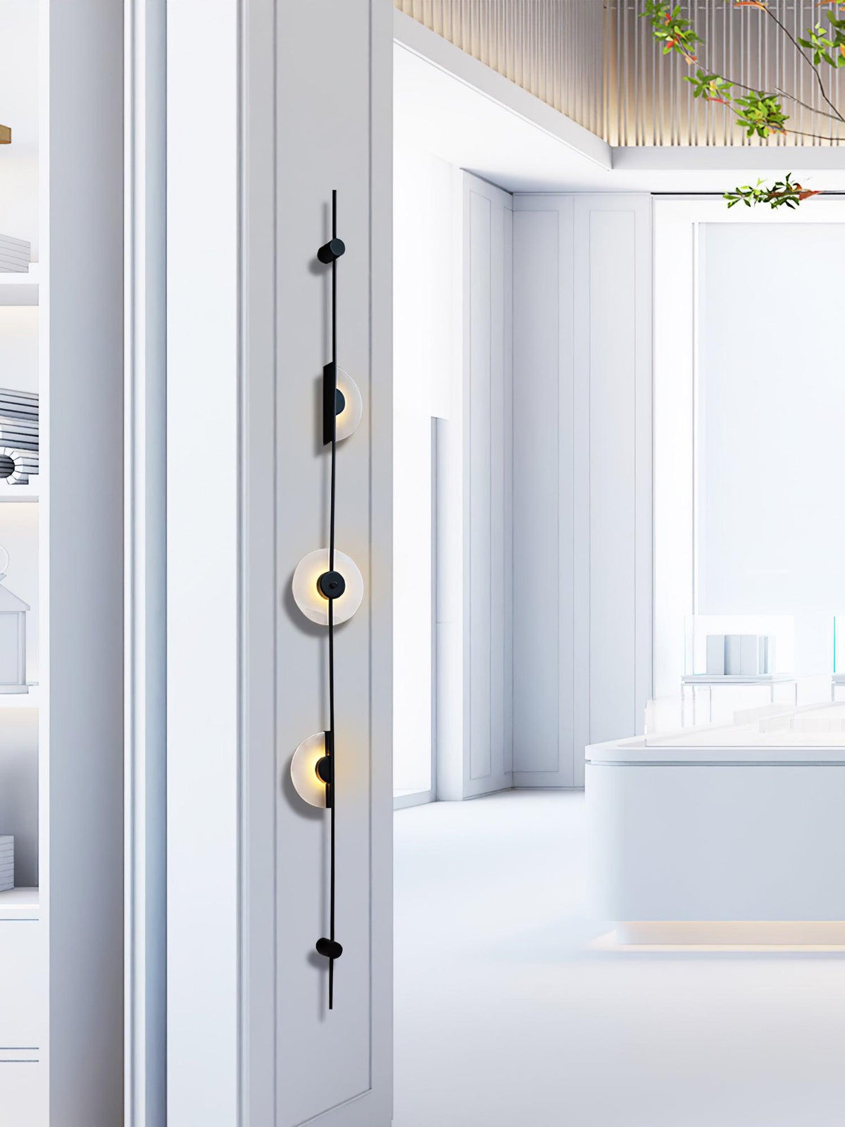 Black three-disc Clérachic sconce on a white wall edge, with a bright, pale showroom space stretching behind it.