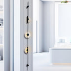 Close, angled view of a black three-disc Clérachic sconce on a white wall, with a pale display space behind.