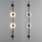 Two black Clérachic sconces side by side on a grey wall, the left lit and the right unlit, each with two alabaster discs.