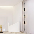 Black three-disc Clérachic sconce on a white wall by a curved white staircase, the discs lit warm.