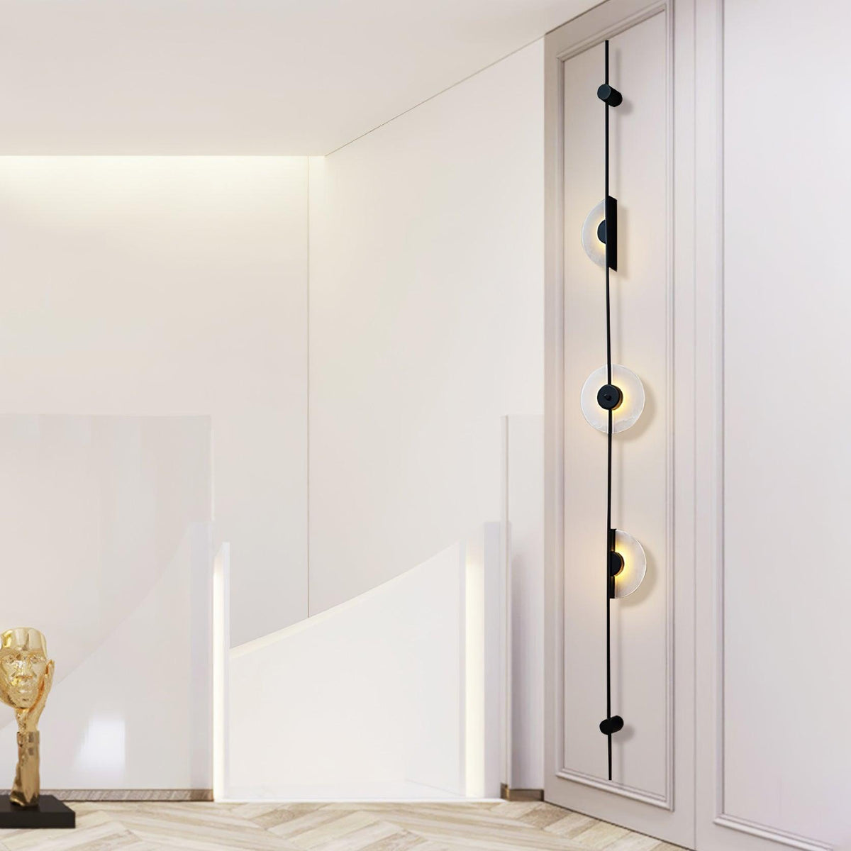 Black three-disc Clérachic sconce on a white wall by a curved white staircase, the discs lit warm.