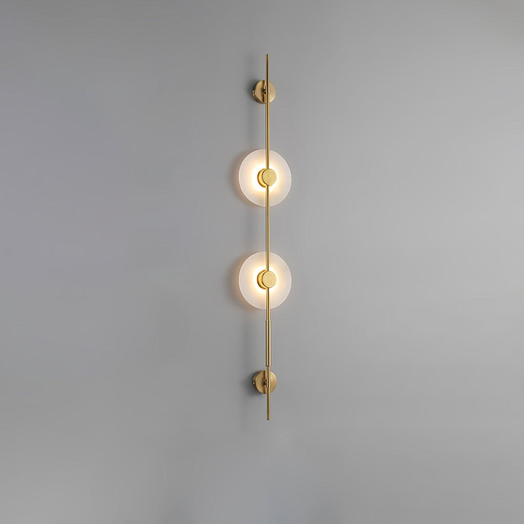 Gold Clérachic sconce with two glowing alabaster discs on a plain grey wall, a slim rod running above and below.