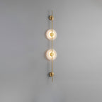 Gold Clérachic sconce with two glowing alabaster discs on a plain grey wall, a slim rod running above and below.