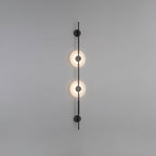 Black Clérachic sconce with two lit alabaster discs on a plain grey wall, with round black caps at both ends.