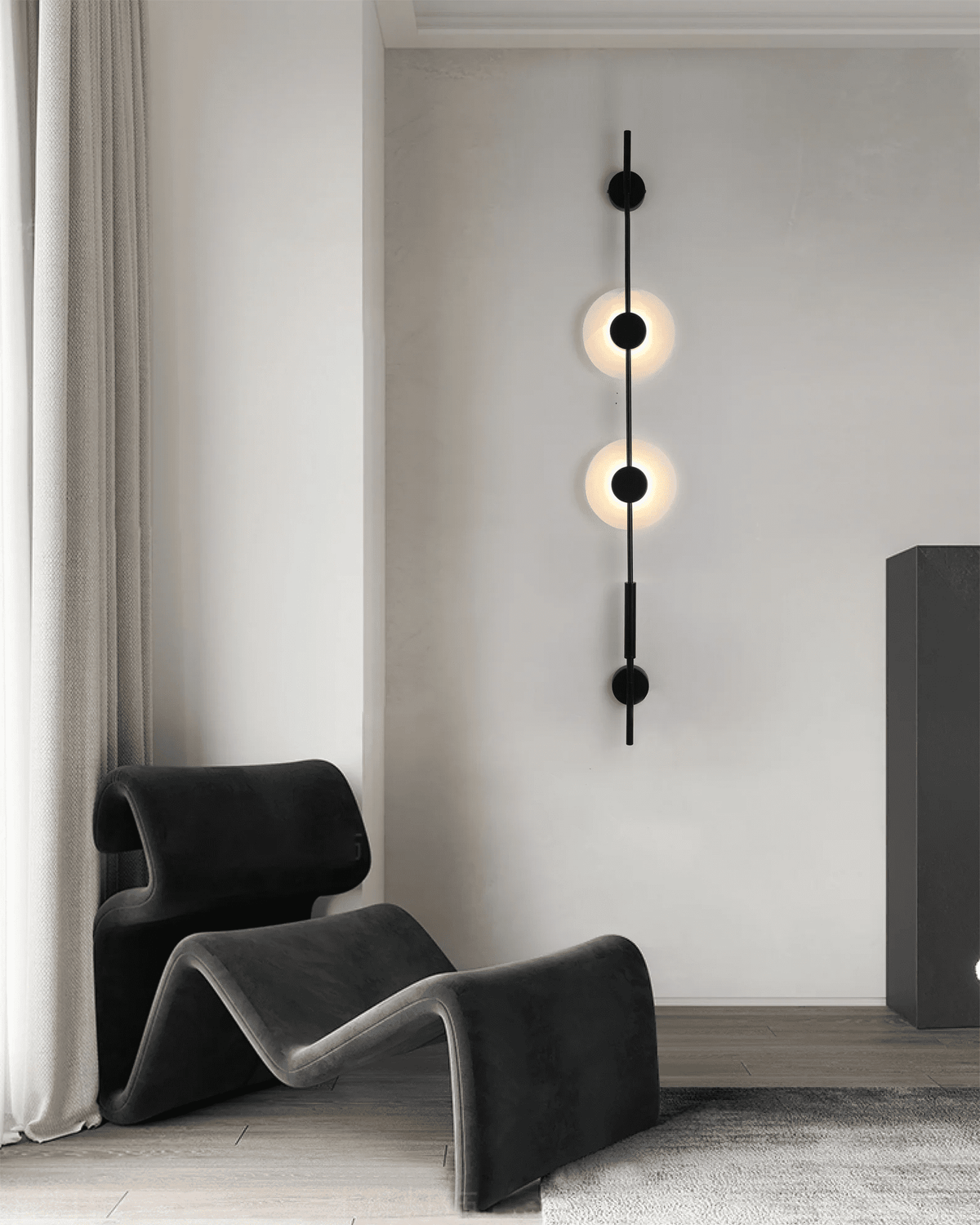 Black Clérachic sconce with two small lit discs on a light wall, above a dark sculpted lounge chair.