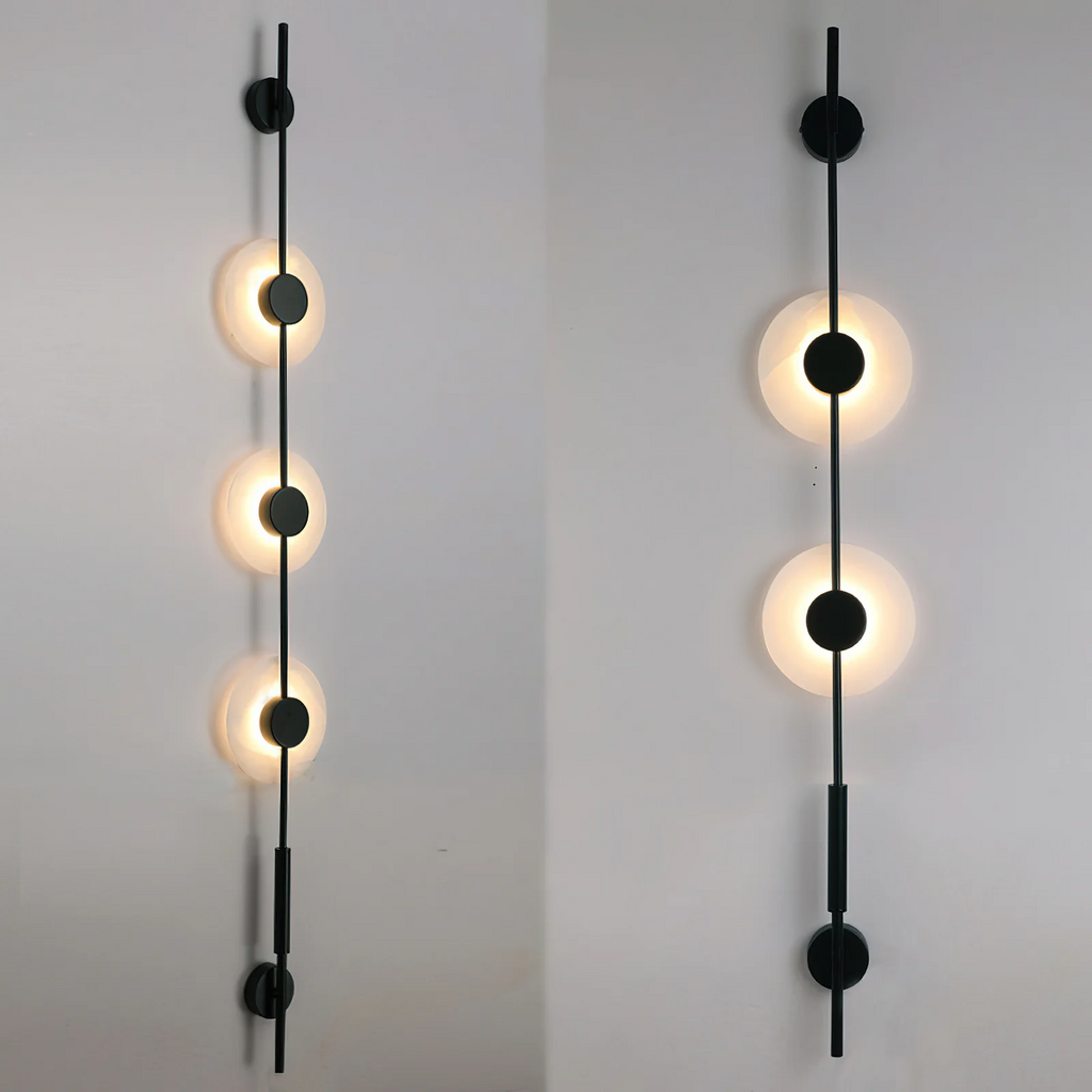 Two black Clérachic sconces on grey: a three-disc model lit on the left and a two-disc model lit on the right.