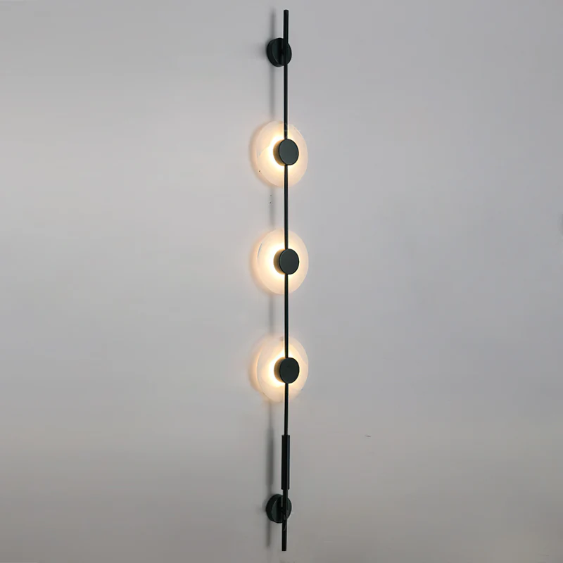 Black three-disc Clérachic sconce with its alabaster discs glowing on a plain grey wall.