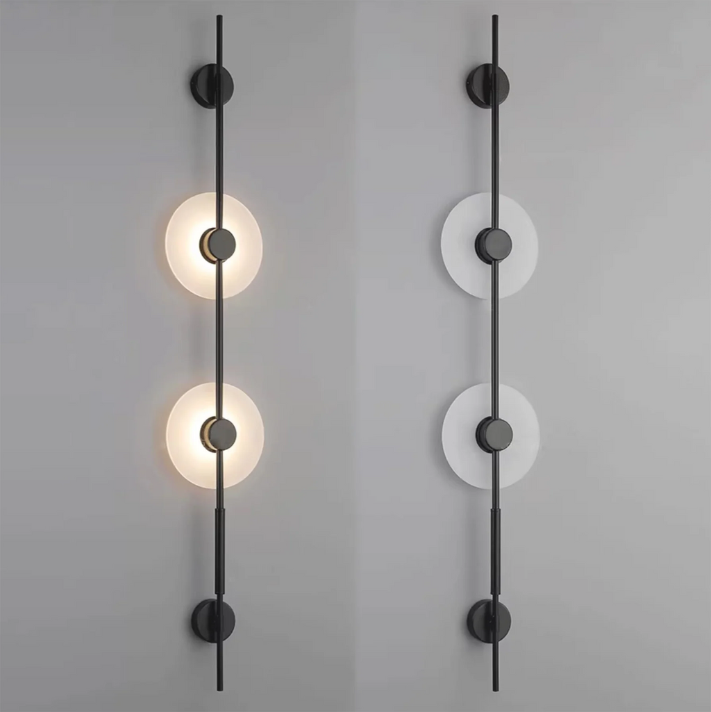 Two black two-disc Clérachic sconces on a grey wall, the left lit and the right unlit to show the pale alabaster.