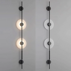 Two black two-disc Clérachic sconces on a grey wall, the left lit and the right unlit to show the pale alabaster.