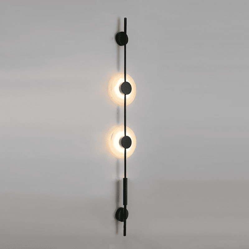 Black Clérachic sconce with two glowing alabaster discs on a soft grey wall, angled slightly from the side.