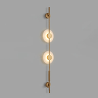 Gold Clérachic sconce with two lit alabaster discs on a grey wall, with small round brass caps at the top and bottom.