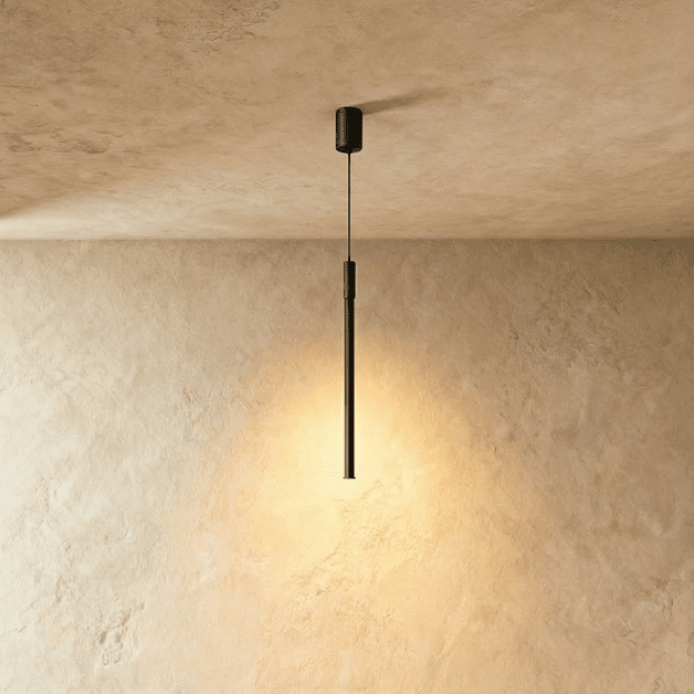 A slim Clérachic black pendant rod drops from a textured ceiling mount, its lower tip glowing warm against plaster.