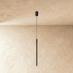 A longer Clérachic black vertical pendant hangs against a plastered corner, its slim rod ending in soft light.