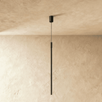 This Clérachic black pendant rod hangs plainly against plaster, its textured cylinder joint catching soft light.
