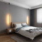 Two Clérachic black rod pendants flank an oak bed, each glowing softly against a gray wall and sheer curtains.