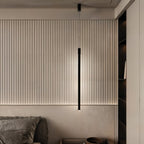 A Clérachic black rod pendant lights a fluted wood headboard panel beside an open bedroom storage nook.