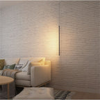 A Clérachic black rod pendant lights a whitewashed brick wall beside a cream sofa with patterned throw pillows.