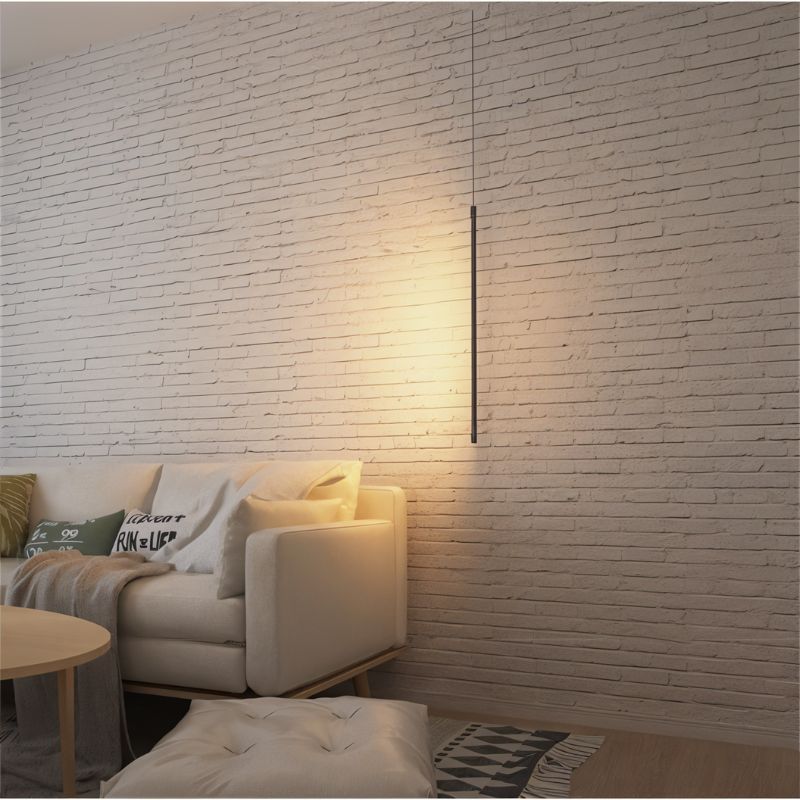 A Clérachic black rod pendant lights a whitewashed brick wall beside a cream sofa with patterned throw pillows.