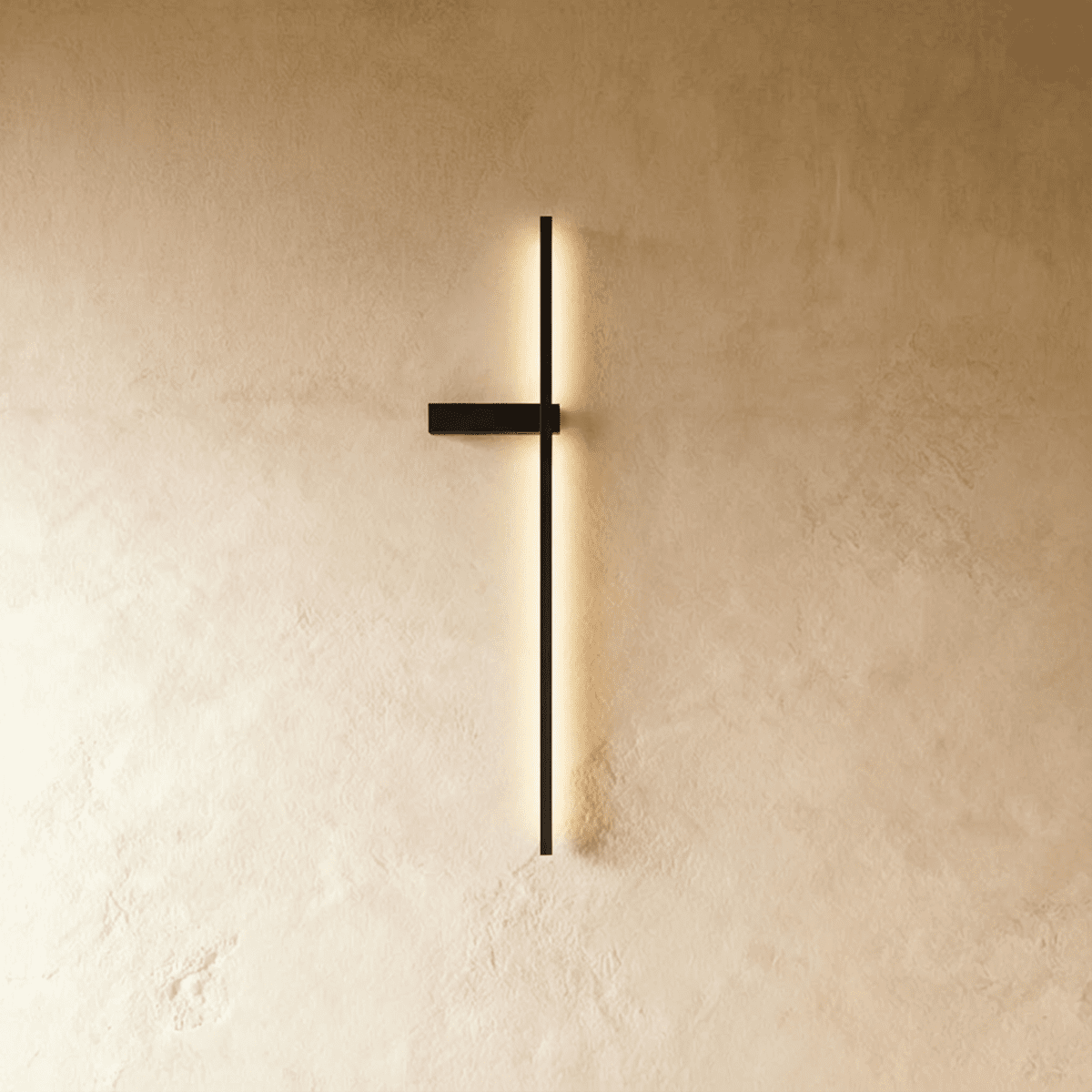Clérachic slim black LED light bar on a limewash wall, its glowing vertical line held by a small horizontal bracket.
