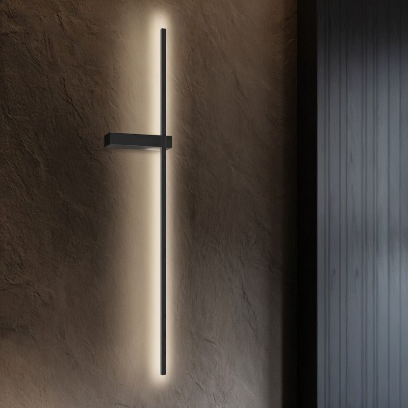 Clérachic tall black LED light bar lit on a dark textured wall, casting a soft warm glow beside a fluted panel.