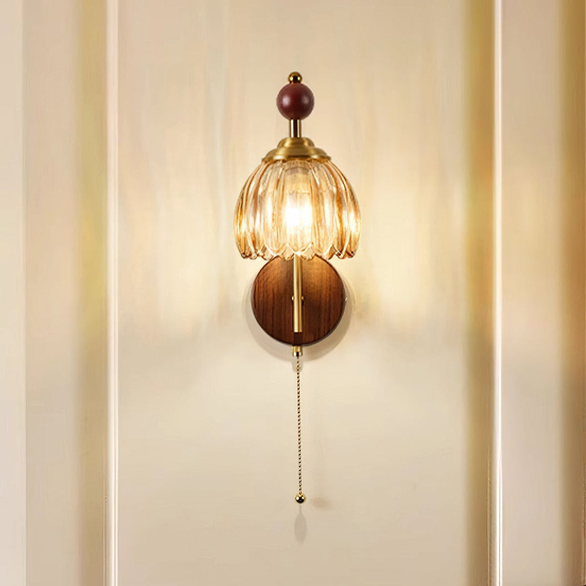 Front view of a Clérachic wall light with a ribbed amber glass shade and a wooden sphere, lit on a cream panelled wall.