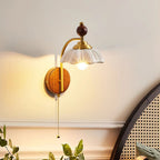 White scalloped-shade Clérachic wall light with a brass arch, lit above a rattan-backed bedhead on a cream wall.