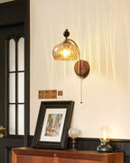 Amber glass Clérachic wall light and a dark-framed print above a wooden cabinet, with a small glass lamp to one side.