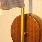 Close view of the round walnut backplate and brass stem of this Clérachic wall light, beneath a white scalloped shade.