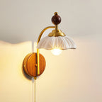 Angled view of a Clérachic wall light with a white scalloped shade, a brass arch and a walnut backplate, lit on a warm wall.
