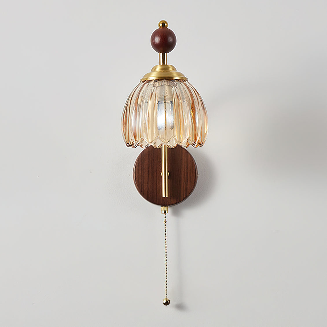 Unlit Clérachic wall light with a ribbed amber glass bell shade, a wooden sphere and a pull chain on a white wall.
