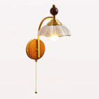 A Clérachic wall light with a scalloped white shade, a brass arm and a pull chain, lit on a white background.