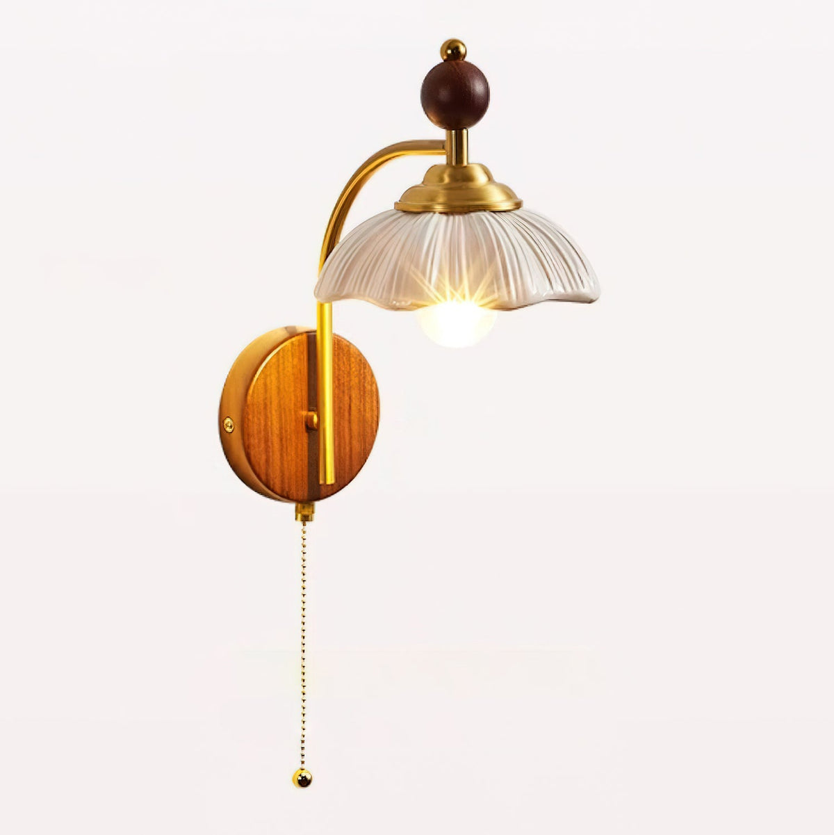 A Clérachic wall light with a scalloped white shade, a brass arm and a pull chain, lit on a white background.