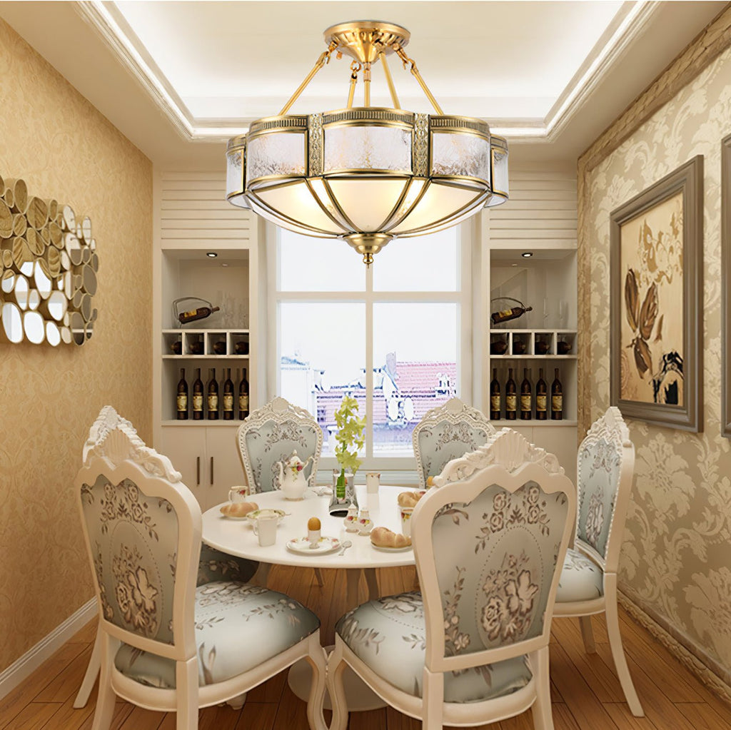 A Clérachic brass ceiling light lit above a small round dining table and floral-backed chairs, in a room with a recessed ceiling glow.