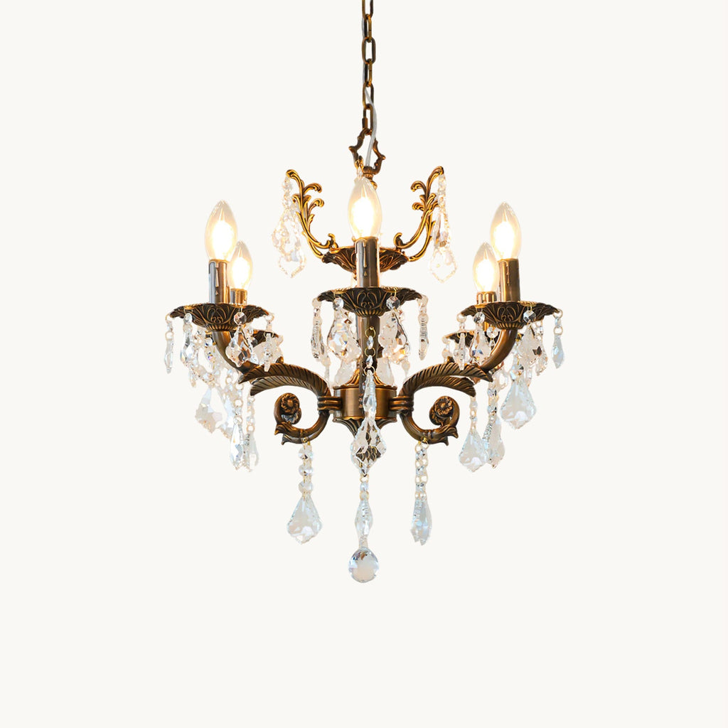 A bronze Clérachic chandelier with scrolled arms, candle bulbs and clear glass prisms, shown lit on a white backdrop.