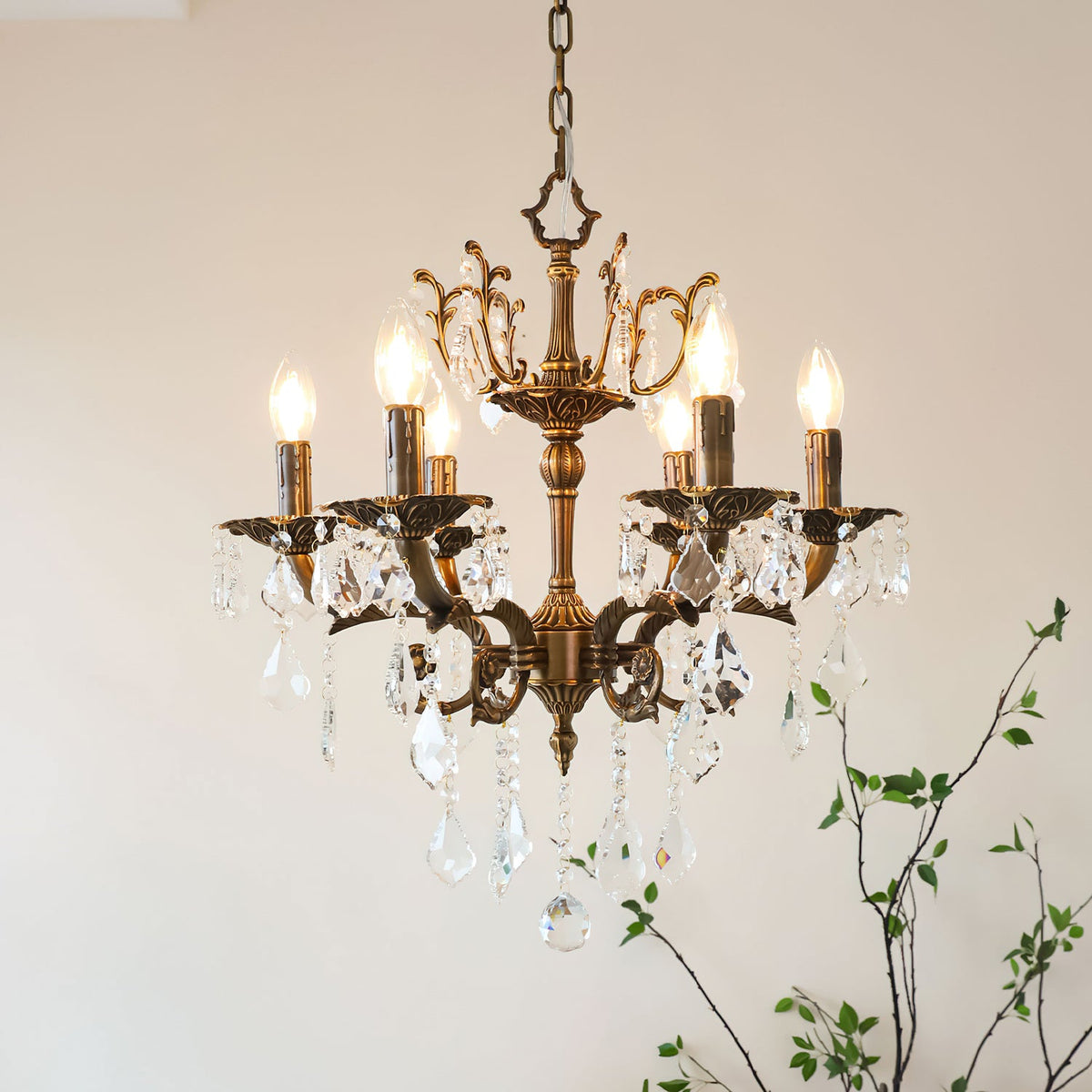 This Clérachic chandelier hangs from a chain against a soft pink wall, its bronze arms and clear prisms catching the light.