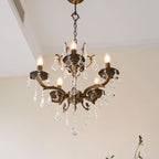 A Clérachic chandelier seen from slightly below, with bronze scrolled arms, clear prisms and warm candle bulbs.