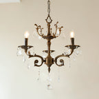 A three-light bronze Clérachic chandelier with scrolled arms and clear prism drops hangs against a plain white wall.