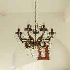 A bronze Clérachic chandelier with eight arms and clear prisms hangs before an arched wall, with a brown mirror behind.
